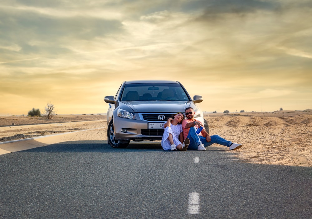 a couple of people sitting on the side of a road next to a car