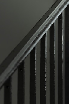 A close-up view of a metal staircase railing with several vertical bars, featuring a dark, muted color scheme.
