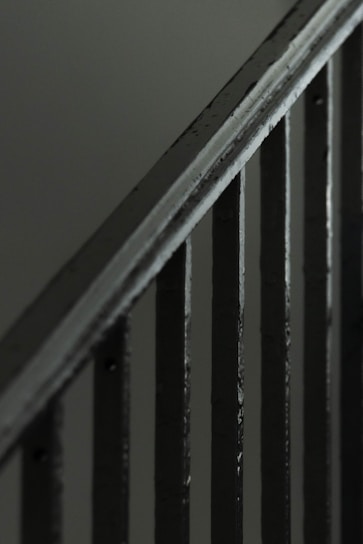 A close-up view of a metal staircase railing with several vertical bars, featuring a dark, muted color scheme.