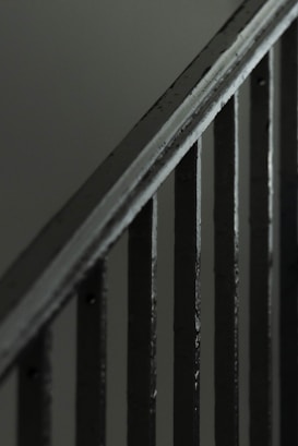 A close-up view of a metal staircase railing with several vertical bars, featuring a dark, muted color scheme.