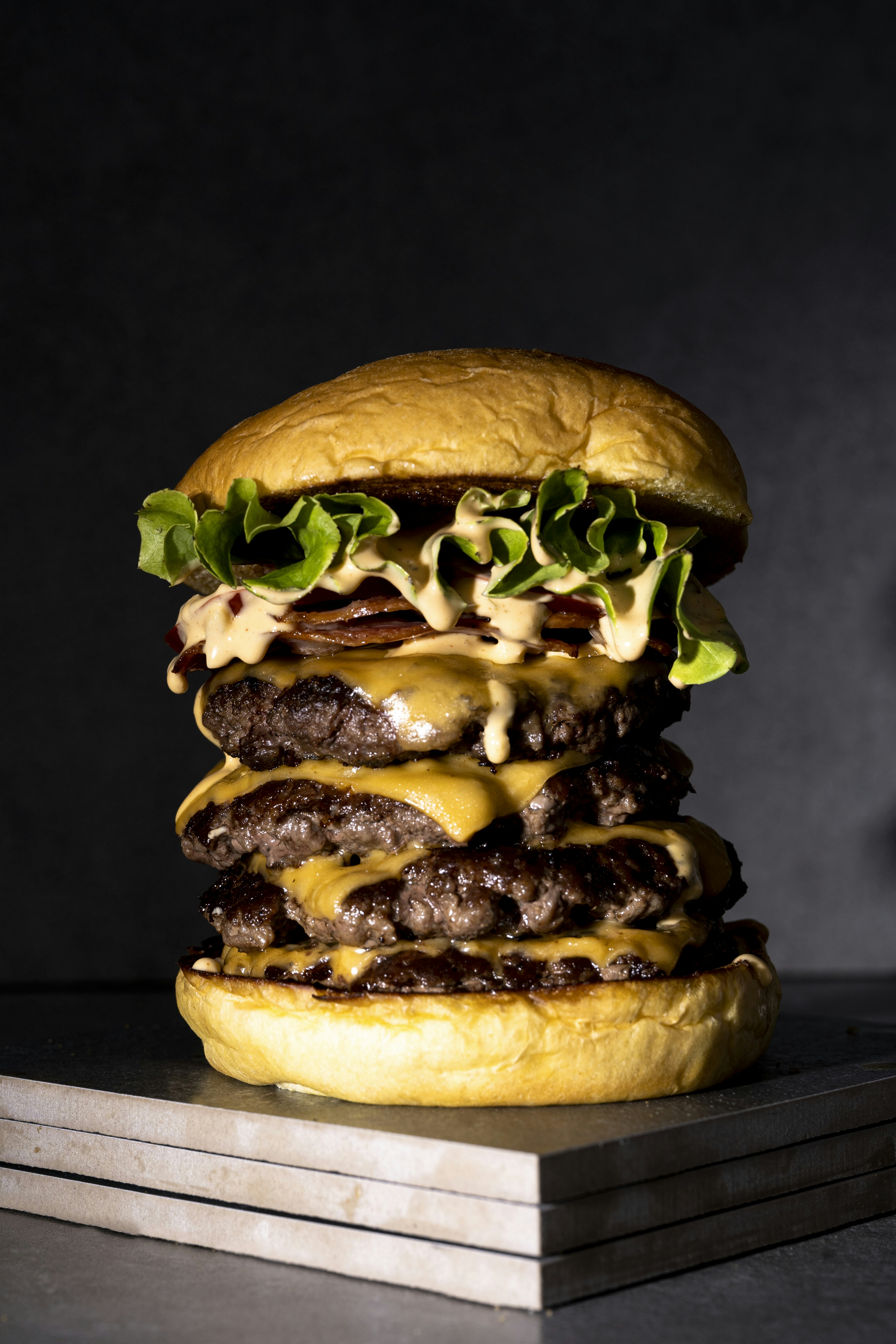 Tall gourmet burger with sesame bun, double patty, cheese, and fresh toppings on dark background