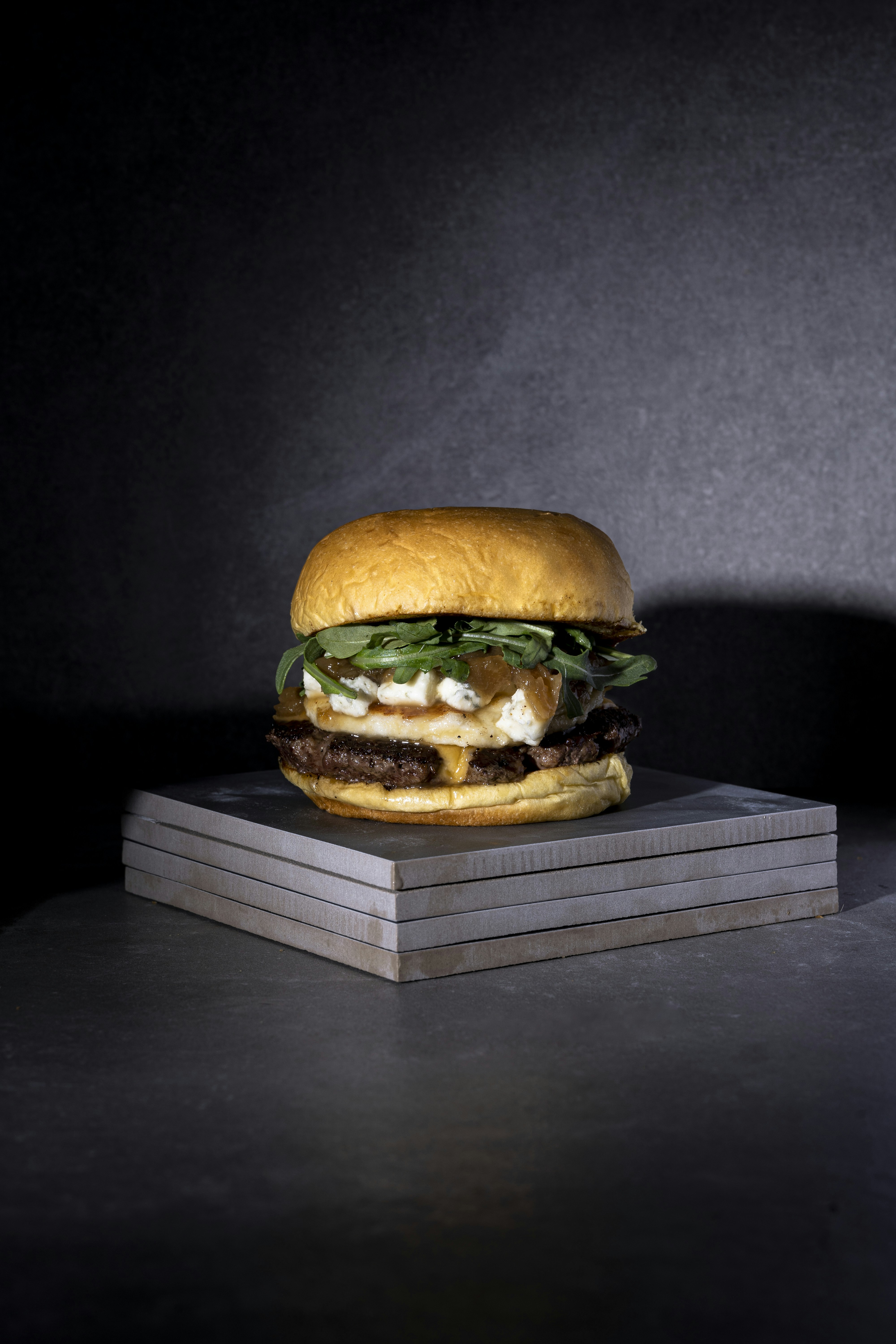 Hamburguesa gourmet con queso derretido y vegetales frescos, fondo oscuro dramático