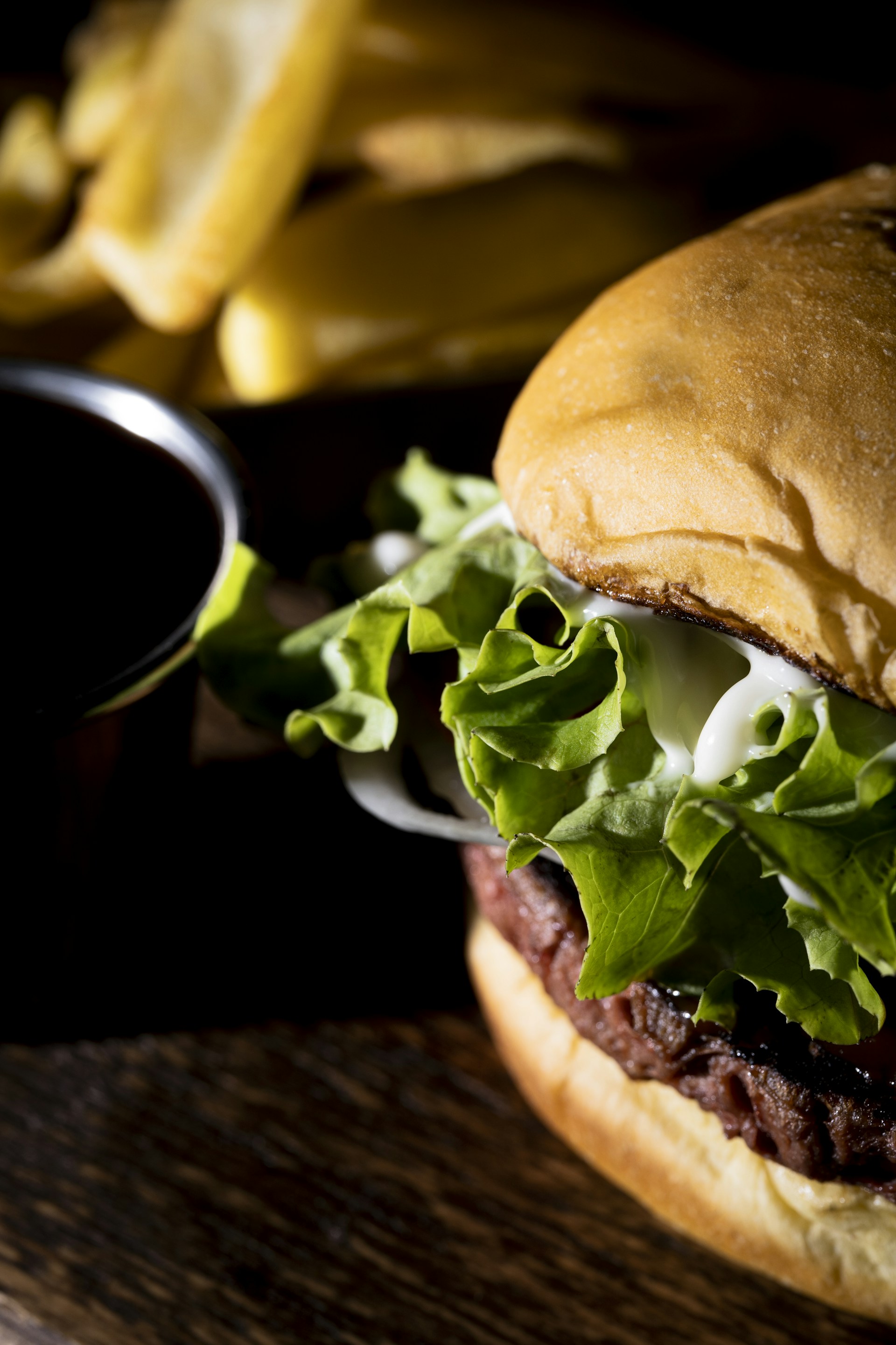 A close-up of a hand holding a loaded burger with fresh lettuce, tomato, and a side of golden fries, capturing the vibrant colors and textures.