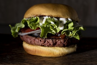 A hamburger with a beef patty topped with fresh green lettuce, slices of tomato, onion, mayonnaise, and ketchup, sandwiched between a golden brown bun.