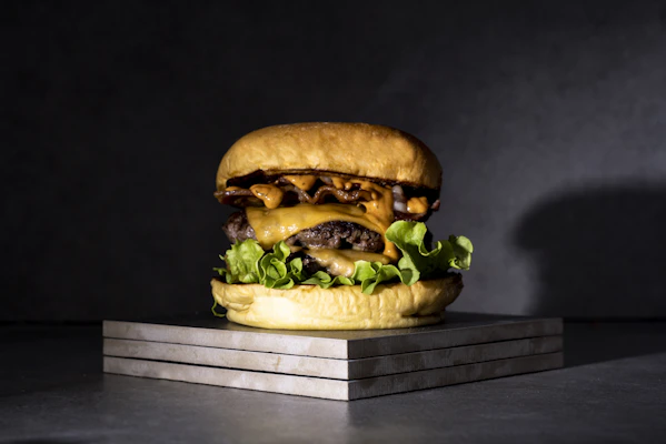Juicy, flame-grilled burgers stacked high with melted cheese and fresh toppings on a dark slate plate.