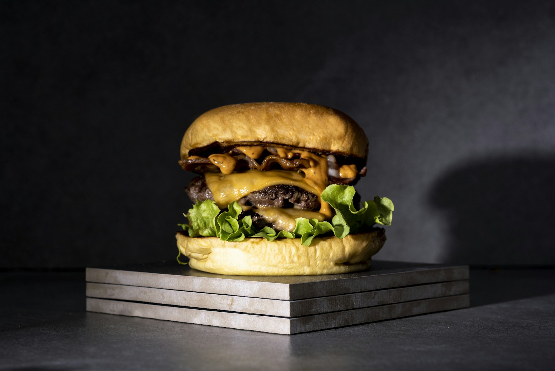 A juicy burger stacked high with melted cheese, fresh lettuce, and tomato, set against a bright yellow background.