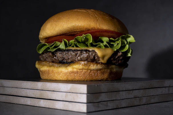Close-up of a juicy grilled beef burger with fresh lettuce and tomato on a rustic wooden board.