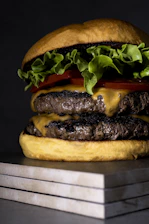 Close-up of a juicy Rokko burger with melted cheddar and fresh lettuce on a black slate background.