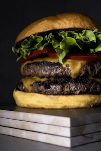 Close-up of a juicy Rokko burger with melted cheddar and fresh lettuce on a black slate background.