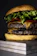 Close-up of a juicy Rokko Burger with melted cheddar and fresh lettuce on a black slate background.