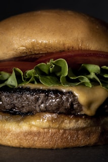 Close-up of a sizzling burger stacked with fresh lettuce, tomato, and melted cheese on a toasted bun