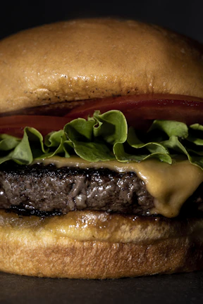 Close-up of a juicy burger with melted cheese and fresh lettuce on a toasted bun.