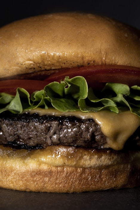 A close-up view of a cheeseburger featuring a juicy beef patty, melted cheese, fresh green lettuce, and a slice of tomato, all nestled in a lightly toasted bun.