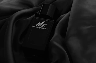 A sleek, dark-themed bottle of premium fragrance glowing softly against a black background.
