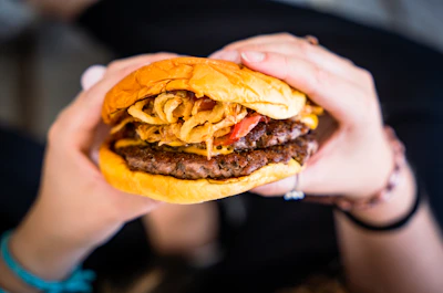 Close-up of a smiling person holding a burger ready to take a bite outdoors.