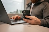 a man sitting in front of a laptop computer holding a cell phone