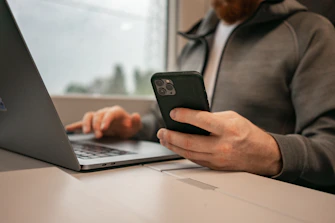 a man sitting in front of a laptop computer holding a cell phone