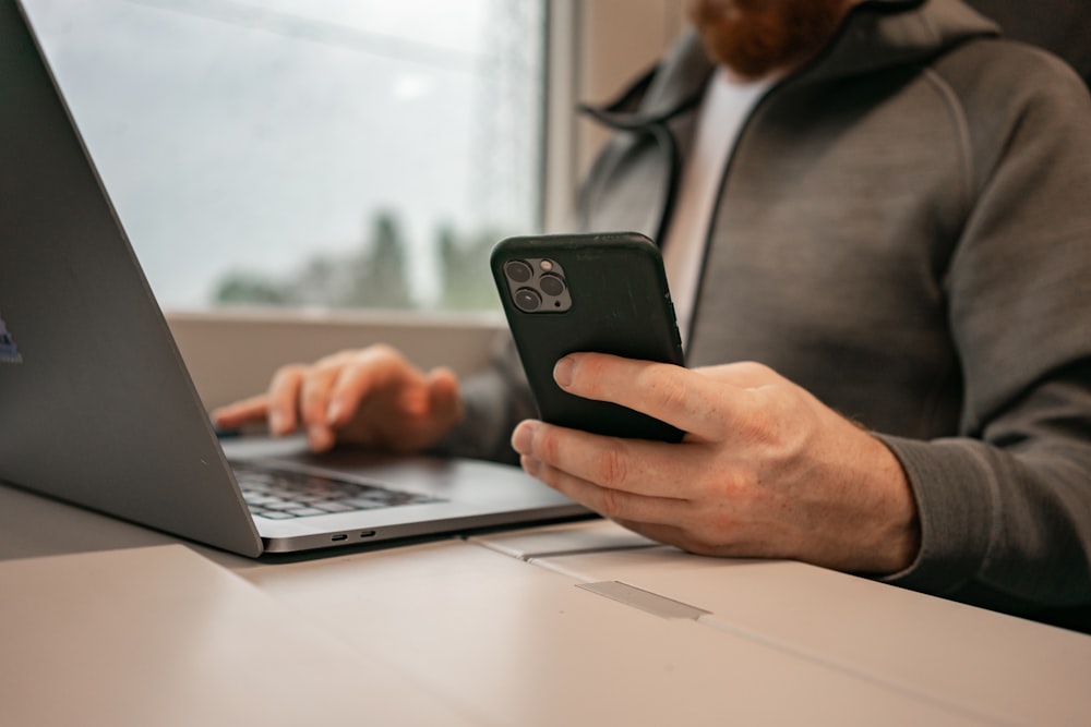 a man sitting in front of a laptop computer holding a cell phone