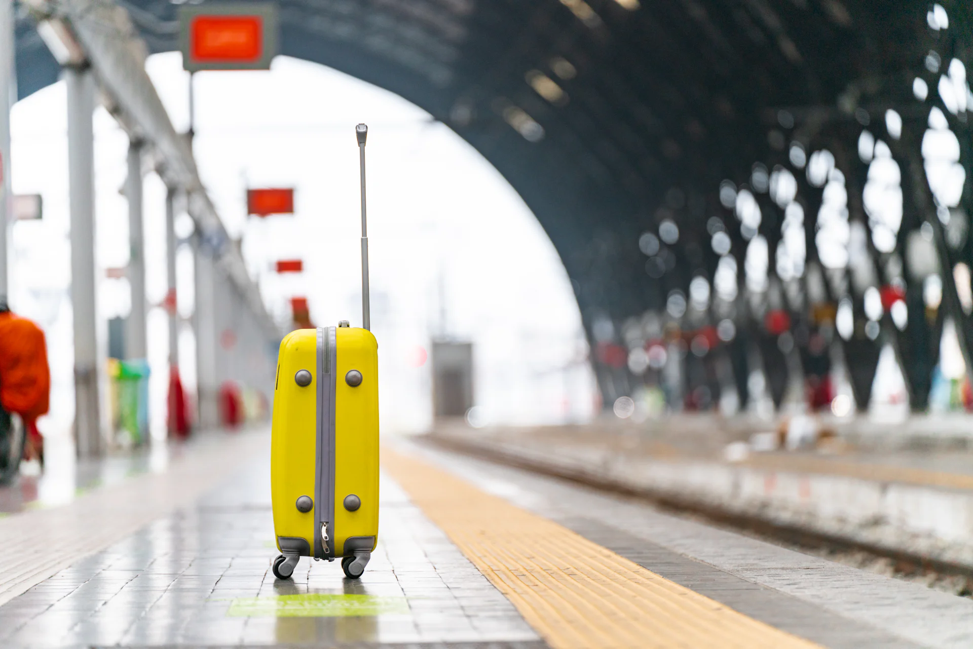A single suitcase standing on a station platform beside the yellow tactile paving