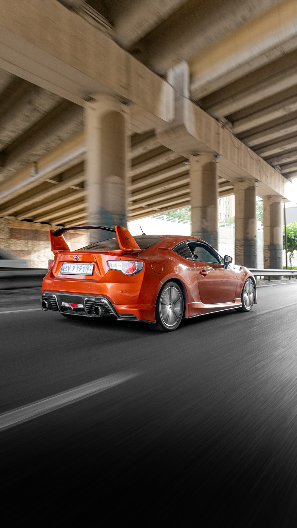 an orange sports car driving under a bridge