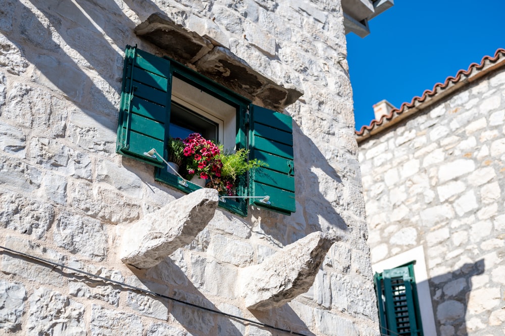 a stone building with green shutters and a window