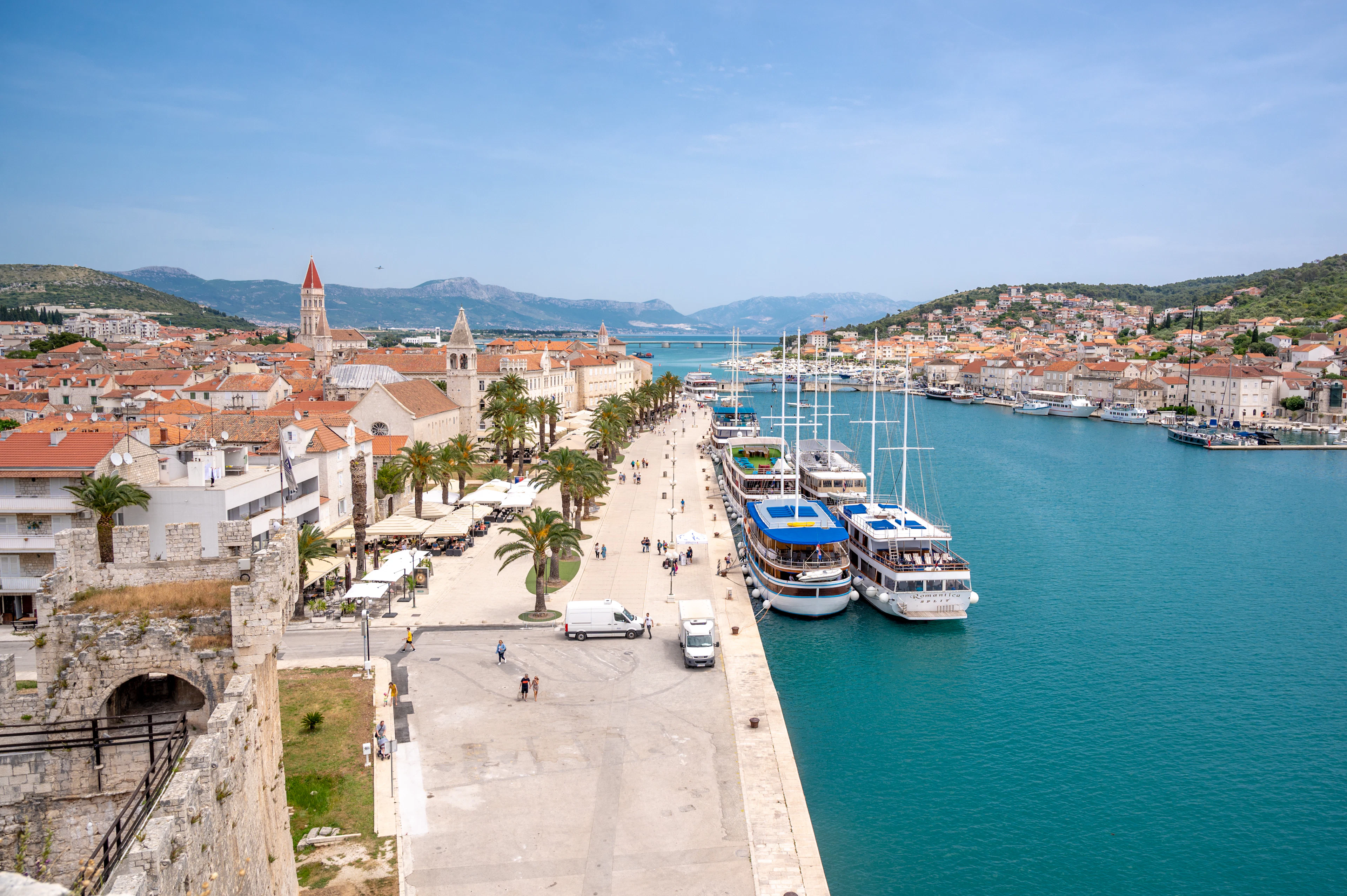 Trogir's palm-lined waterfront, old-town roofs and moored boats, seen from the fortress walls