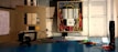 An open electrical panel with a multitude of colorful wires connected to various circuit breakers is mounted on a wall. Tools are placed on a blue workbench, including a multimeter and a screwdriver. A visible checklist is attached to the left panel door.