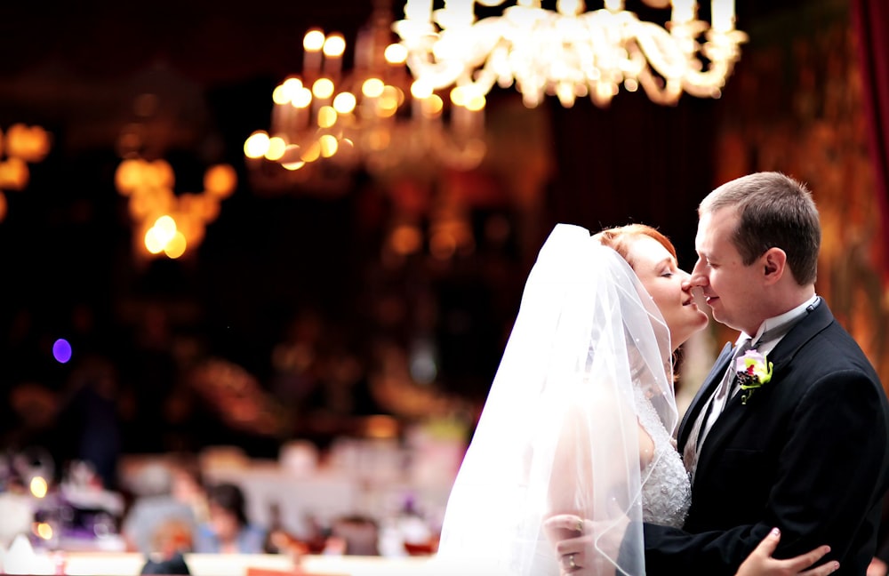 a bride and groom kissing in front of a chandelier