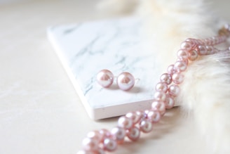 a pink pearl necklace and matching earrings on a marble surface
