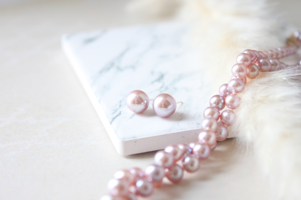 a pink pearl necklace and matching earrings on a marble surface