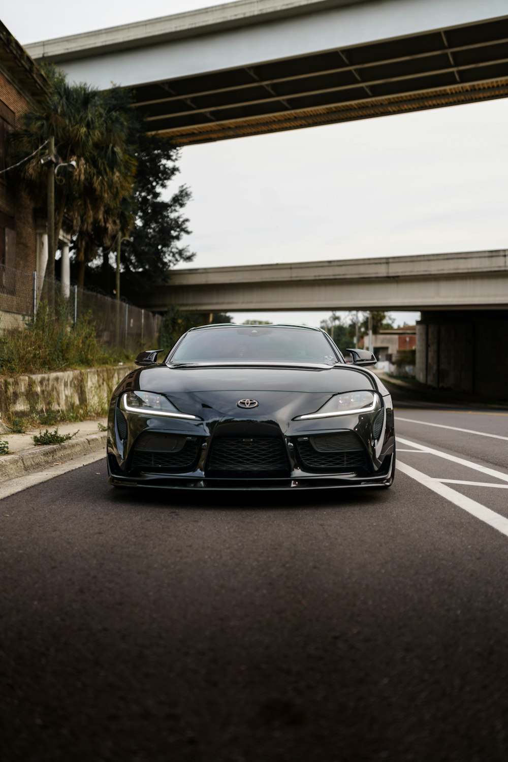 a black sports car driving down a street under a bridge