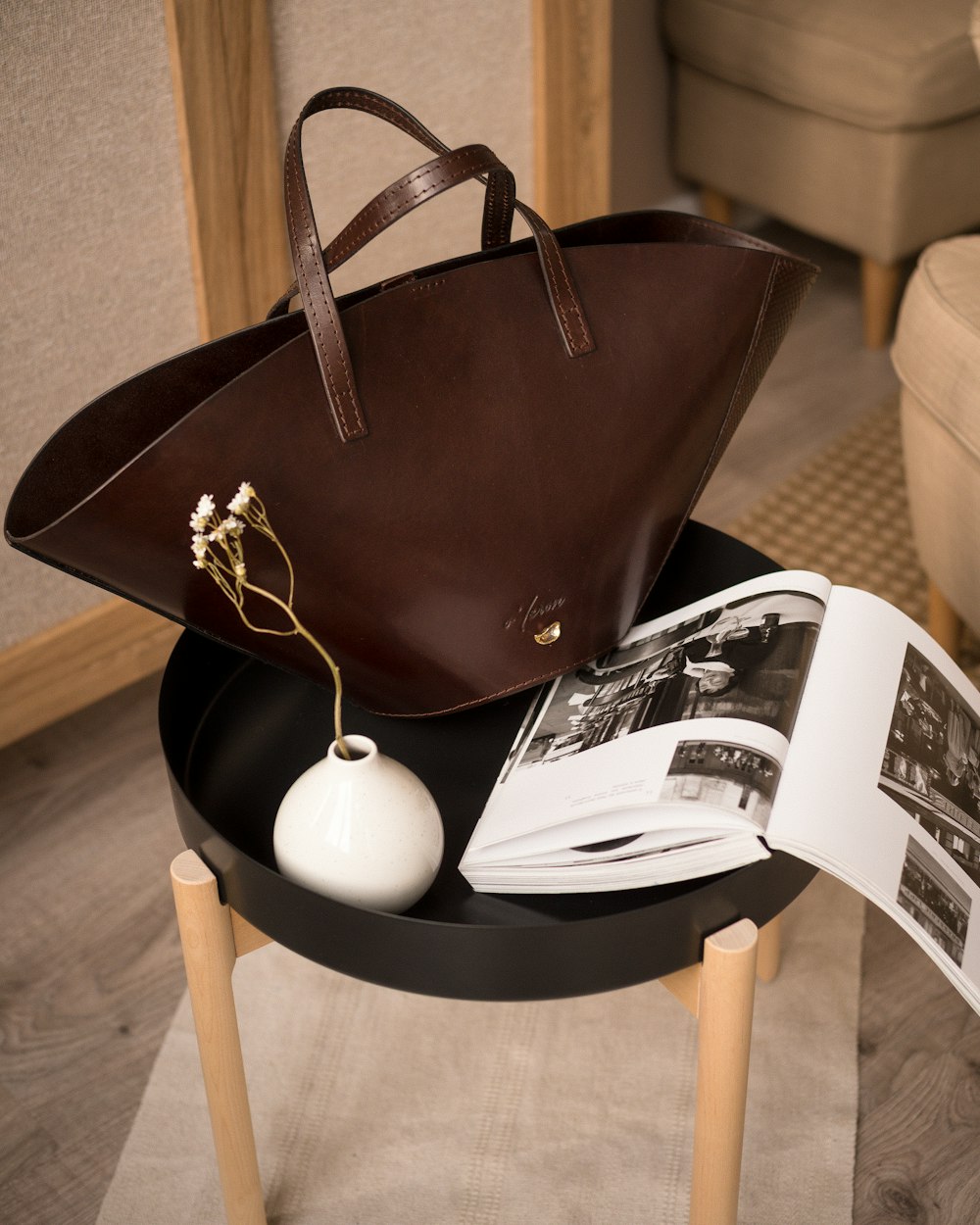Un bolso marrón sentado encima de una mesa junto a un libro abierto