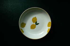 A bright yellow ceramic plate filled with fresh fruit, set on a linen cloth with soft natural light.