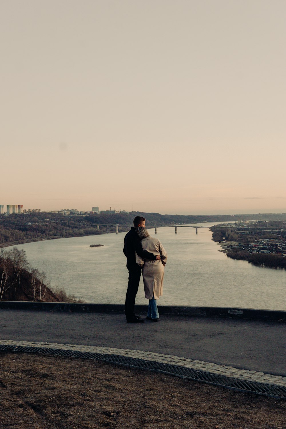 a man and a woman standing on a hill overlooking a body of water