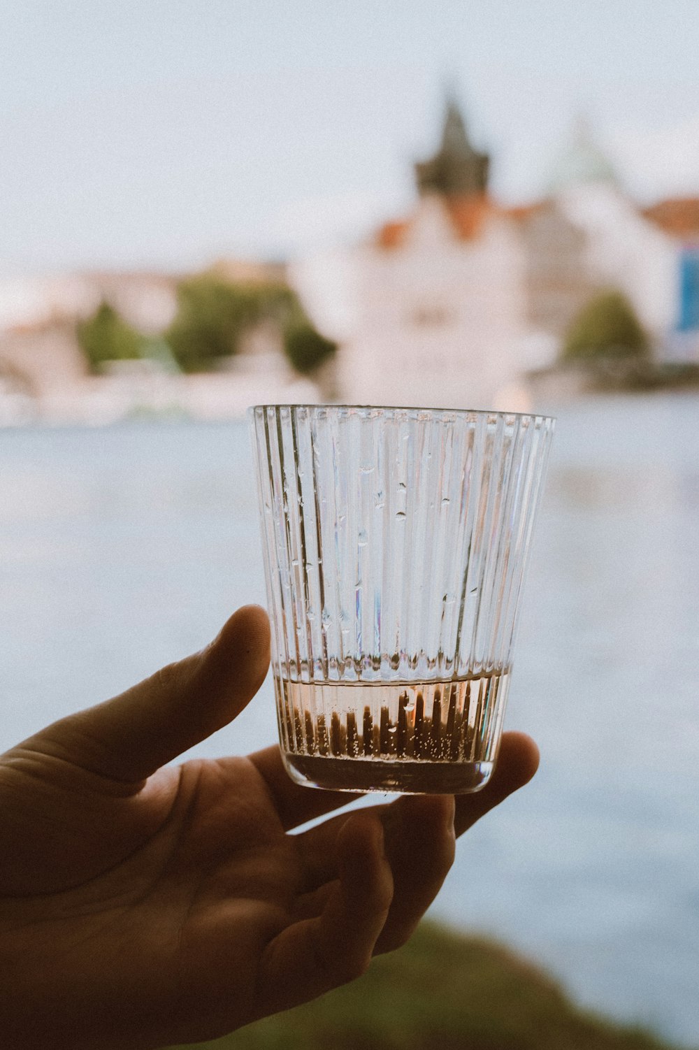 a hand holding a shot glass in front of a body of water