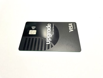 A credit card lies flat against a plain white background. The card features a sleek, minimalist design in dark and metallic shades. The word 'upgrade' is prominently featured along with text indicating Visa Signature.