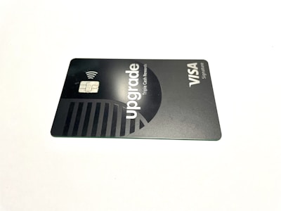 A credit card lies flat against a plain white background. The card features a sleek, minimalist design in dark and metallic shades. The word 'upgrade' is prominently featured along with text indicating Visa Signature.