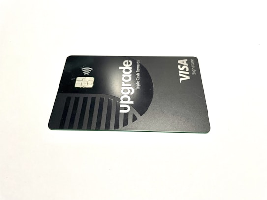 A credit card lies flat against a plain white background. The card features a sleek, minimalist design in dark and metallic shades. The word 'upgrade' is prominently featured along with text indicating Visa Signature.