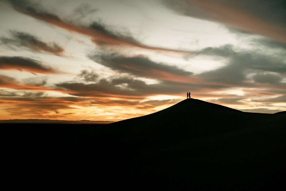 une personne debout au sommet d’une colline au coucher du soleil