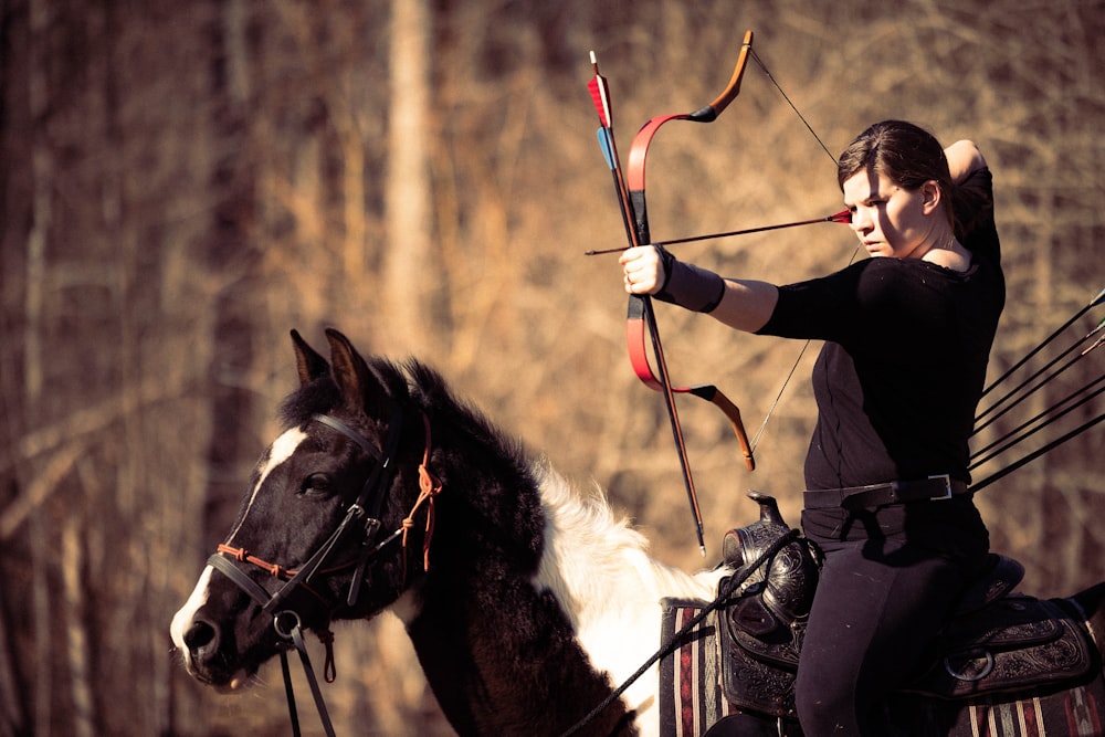 a woman riding on the back of a horse holding a bow and arrow