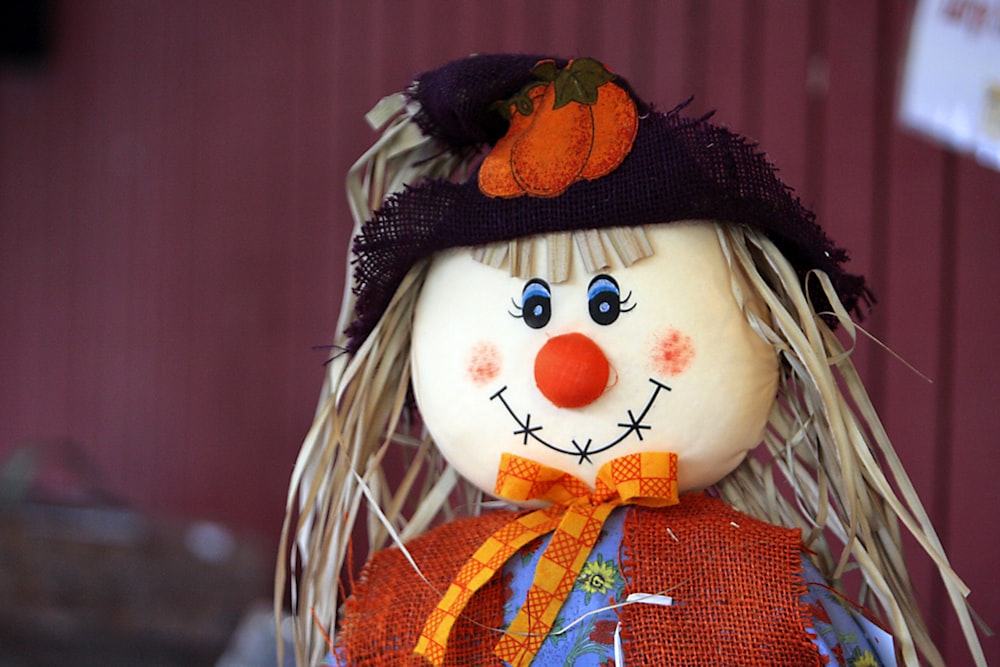 une poupée épouvantail avec un chapeau noir et une écharpe orange
