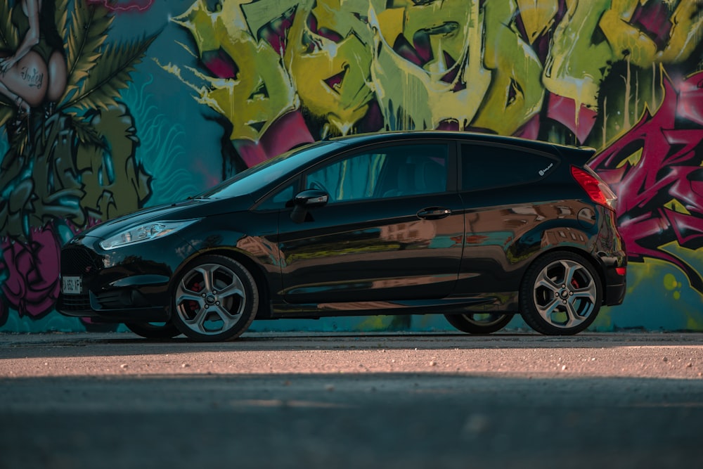 a black car parked in front of a graffiti covered wall