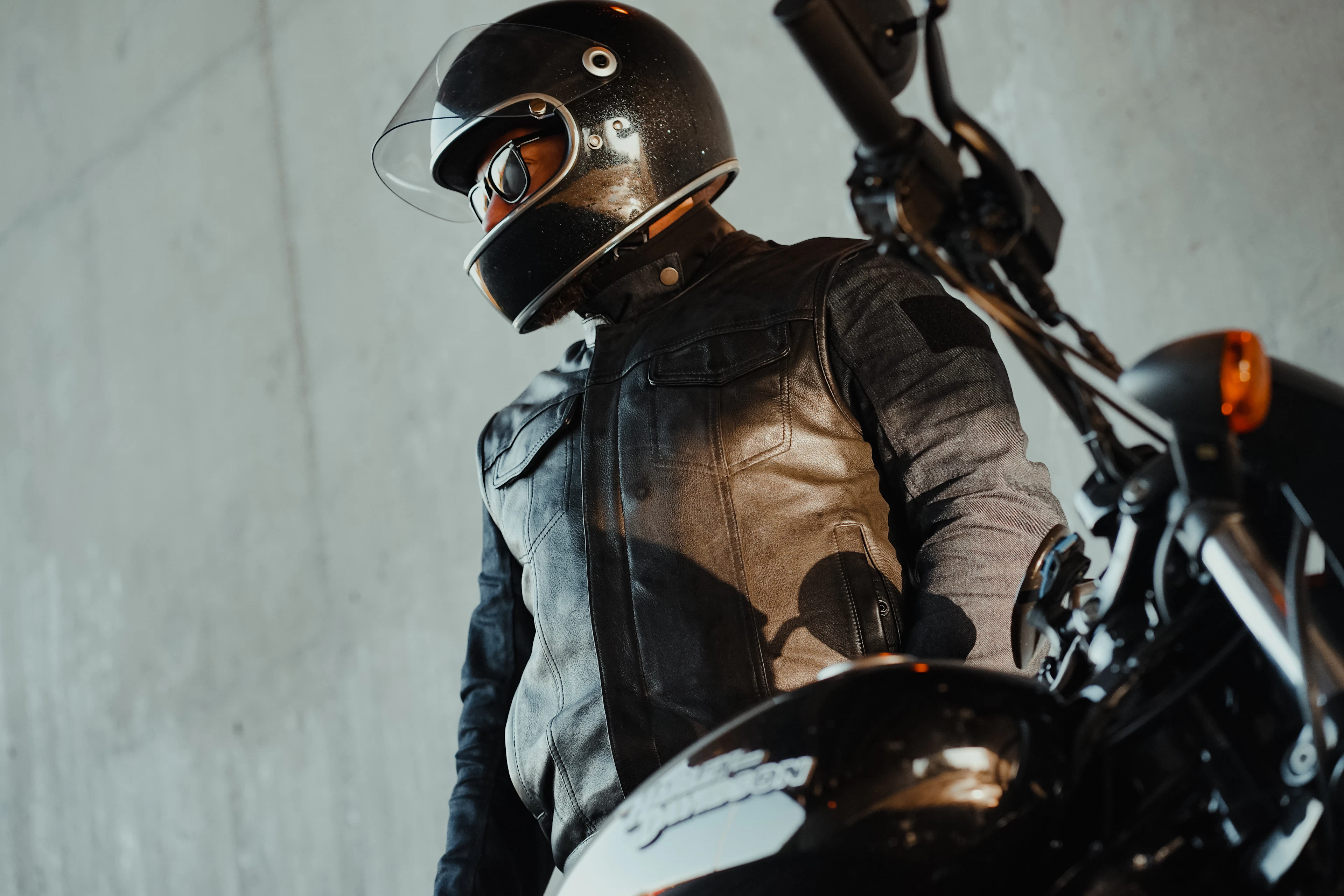 Rider wearing a brown and black leather riding jacket beside a motorcycle