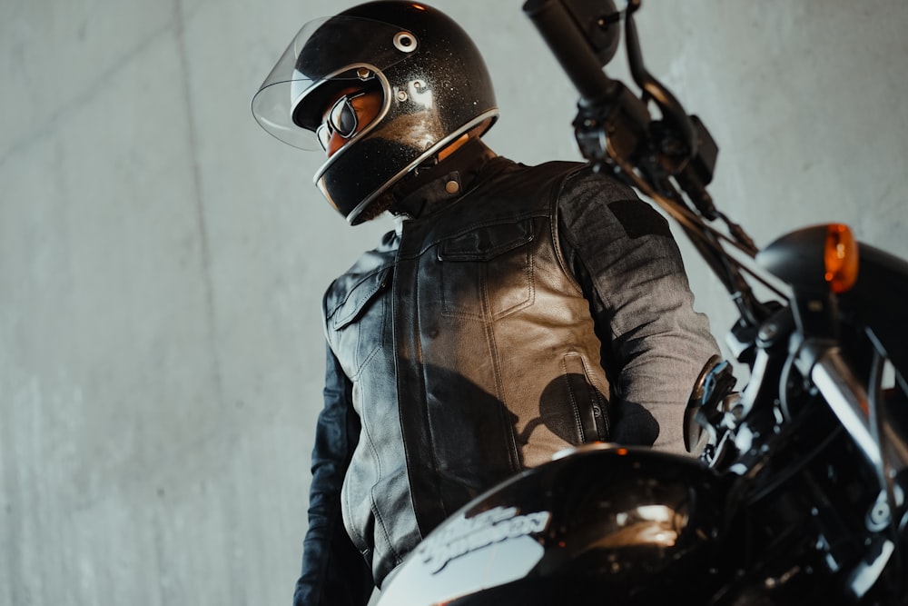 a man in a leather jacket and helmet standing next to a motorcycle