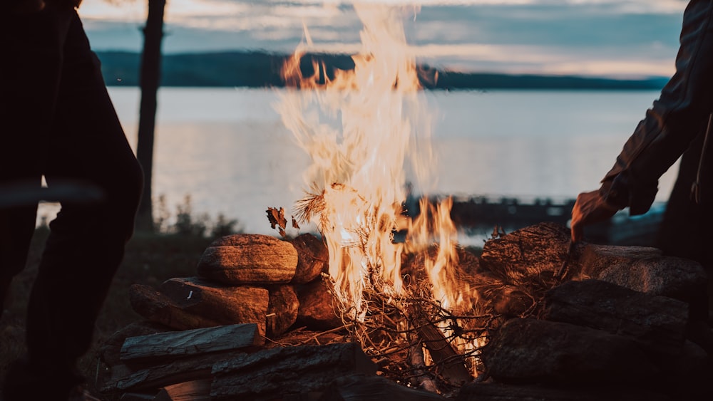 a person standing next to a fire with a lake in the background