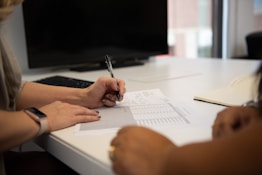 two people sitting at a desk writing on a piece of paper