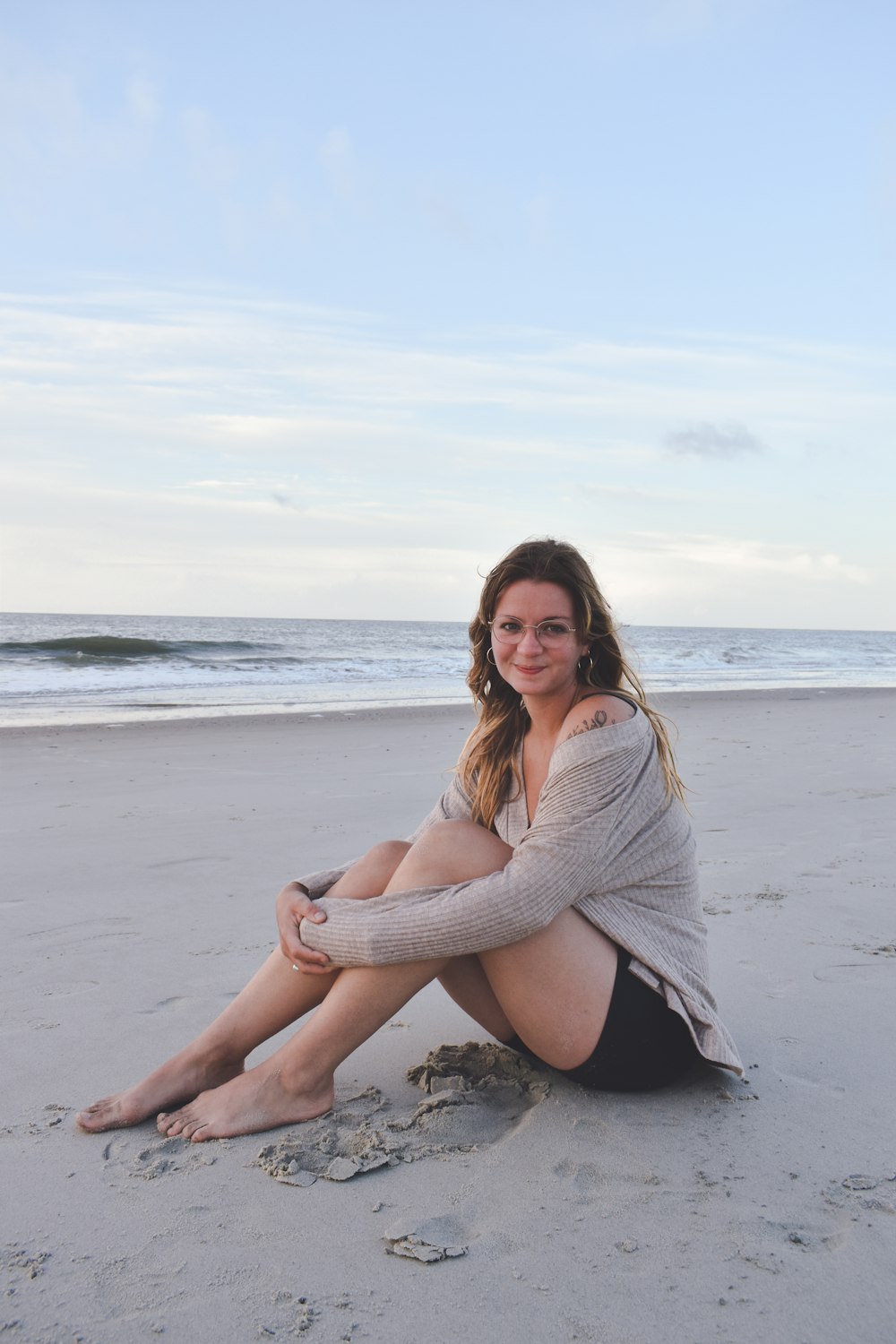 a woman sitting on the beach with her legs crossed