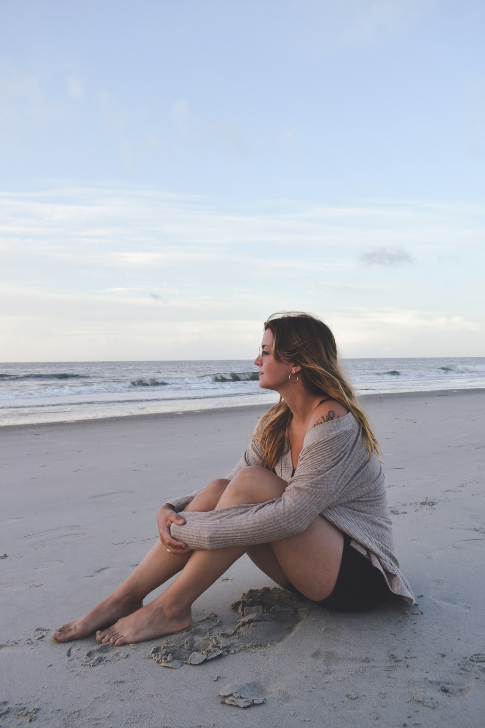 a woman sitting on the beach with her legs crossed