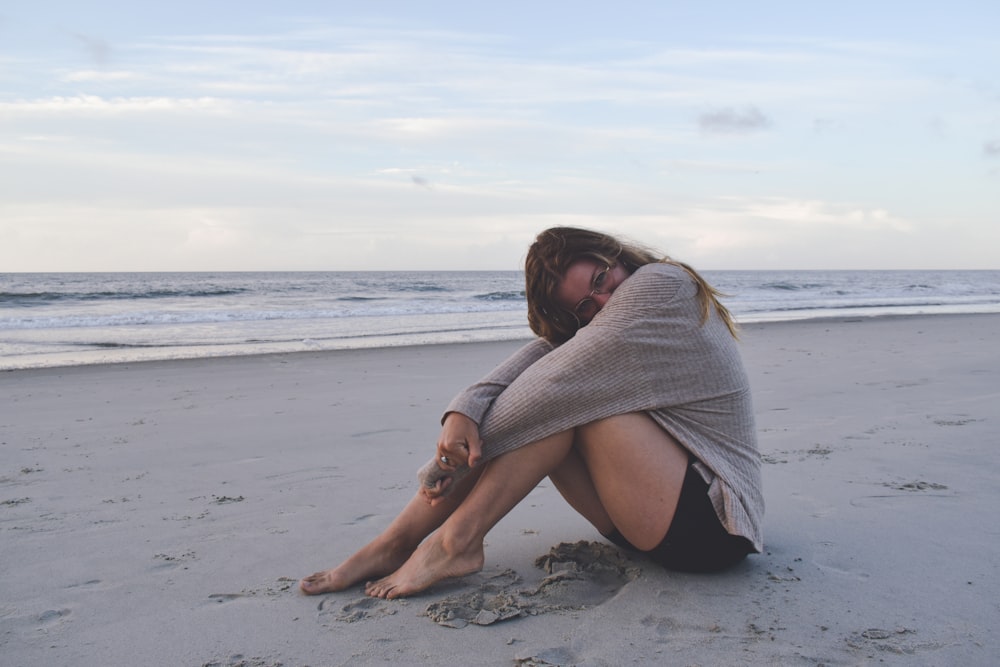 a woman sitting on the beach with her legs crossed