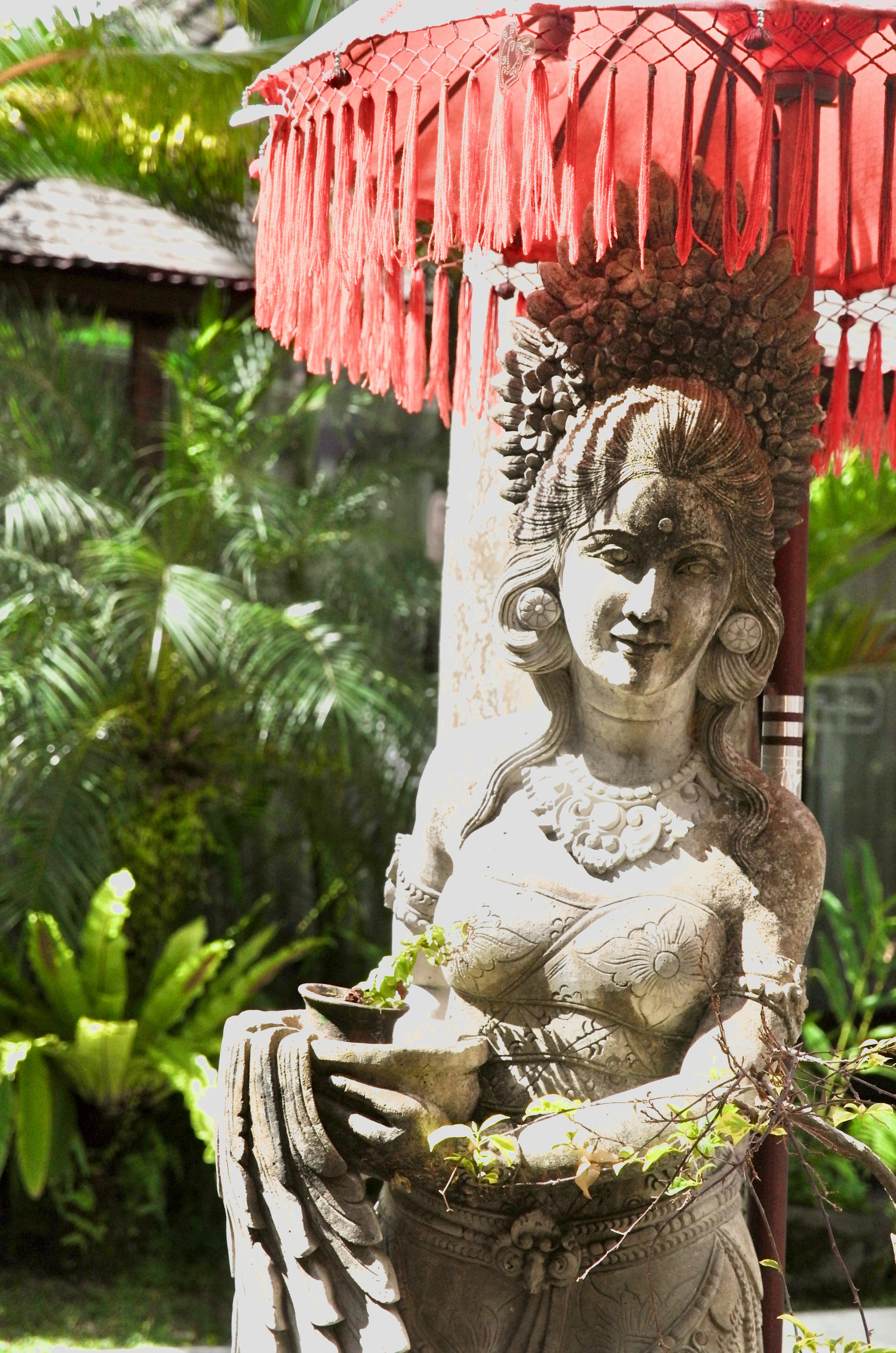 a statue of a woman holding a basket under a red umbrella